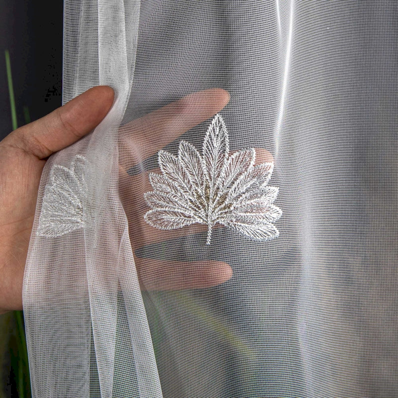 a person's hand holding onto a sheer curtain with a leaf embroidered on it