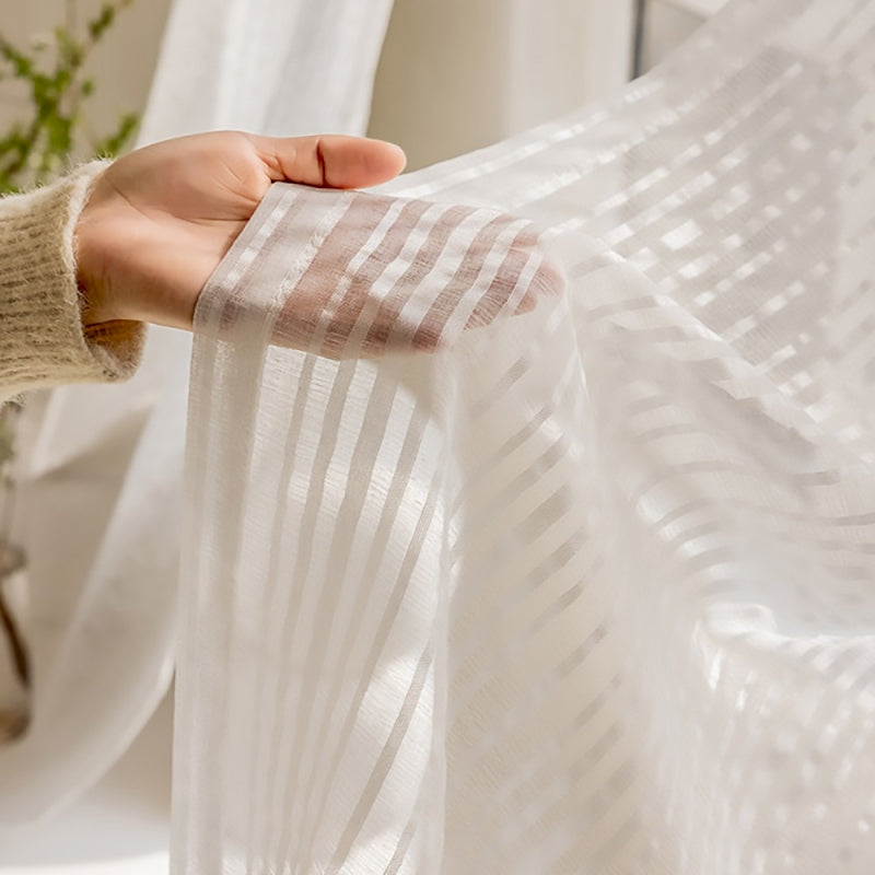 a person's hand holding a white curtain in front of a window