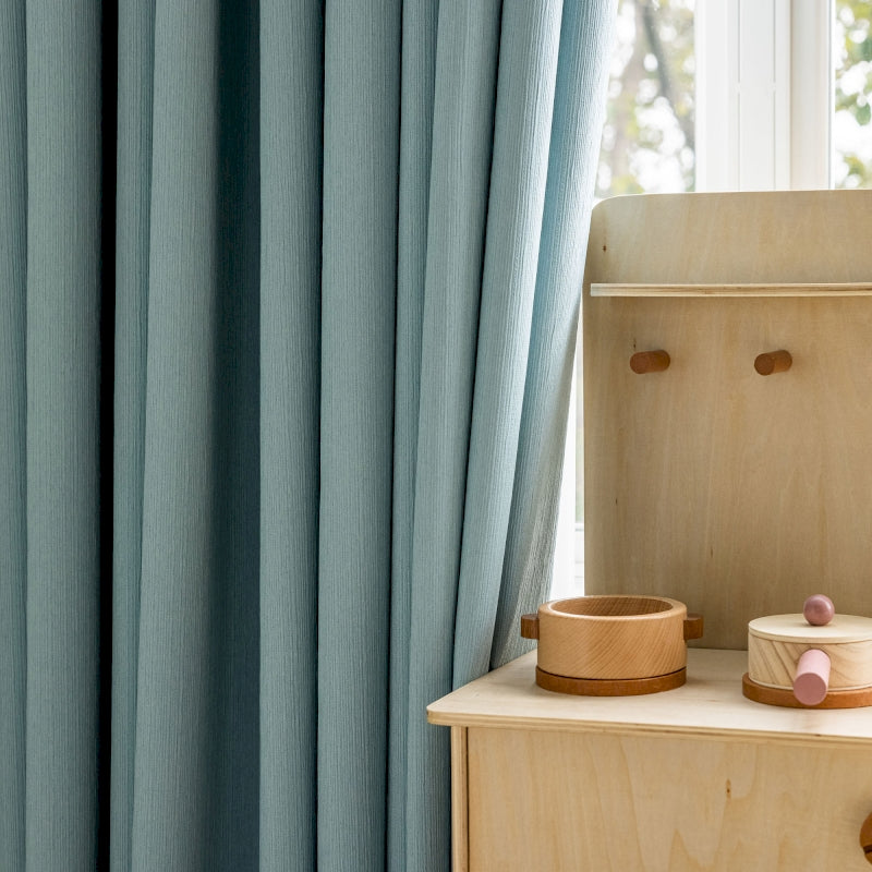 a child's room with blue curtains and a wooden dresser