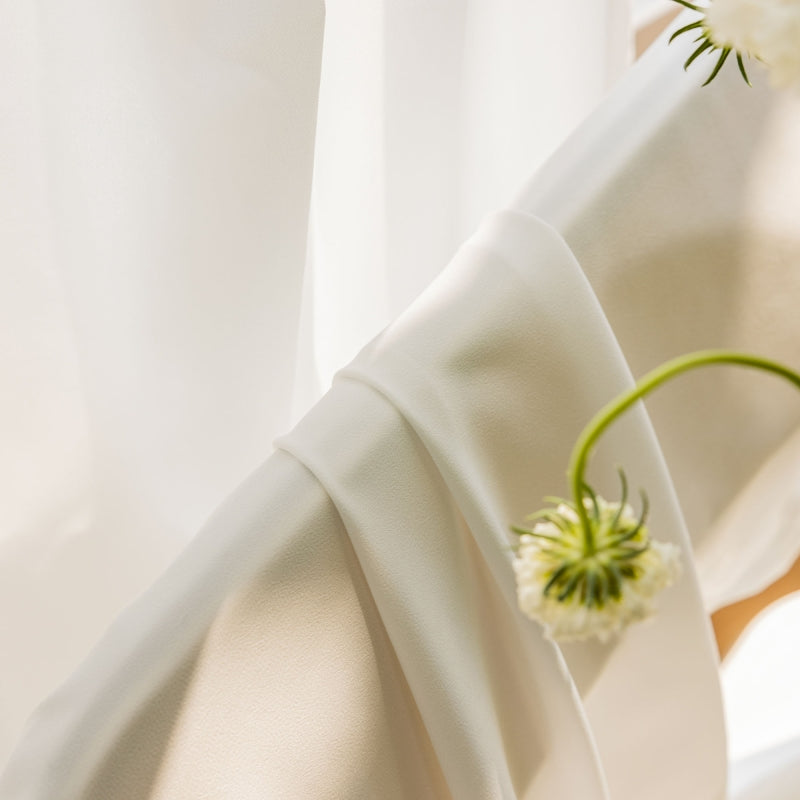 two white flowers sitting on top of a white curtain